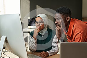 Two young serious intercultural IT engineers looking at computer screen