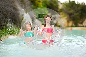 Two young sisters bathing in natural swimming pool in Bagno Vignoni, with thermal spring water and waterfall. Tuscany, Italy