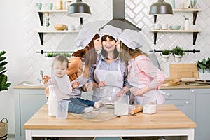 Two young sisters, grandmother and little baby daughter having good time in the kitchen. Daughters are kissing their