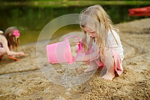 Two young sisters having fun on a sandy lake beach on warm and sunny summer day. Kids playing by the river