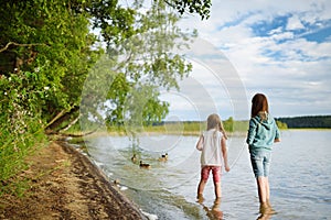 Two young sisters having fun on a sandy lake beach on warm and sunny summer day. Kids playing by the river