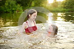 Two young sisters having fun on a sandy lake beach on warm and sunny summer day. Kids playing by the river