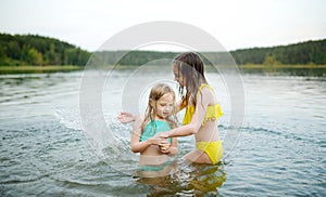 Two young sisters having fun on a sandy lake beach on warm and sunny summer day. Kids playing by the river