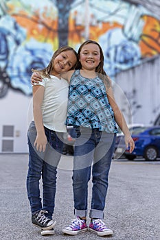 Two young sisters hold each other side by side in a colorful outdoor parking lot