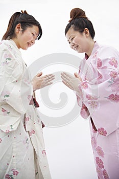 Two young smiling woman in Japanese kimonos bowing to each other, studio shot