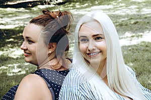 Two young smiling women sit side by side in the park