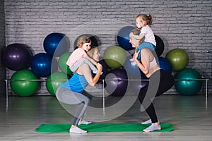 Two young sports mom and baby girls do exercises together in the