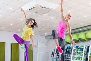 Two young sporty women exercising in fitness studio, dancing, doing cardio, working on balance and coordination.