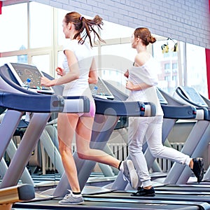 Two young sporty women run on machine