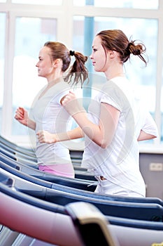 Two young sporty women run on machine