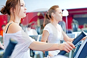 Two young sporty women run on machine