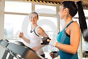 Two young sporty women run on machine in the gym center