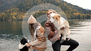 Two Young stylish Caucasian female women playing with her border collie puppy outdoors on lake in mountain. travel