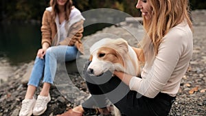 Two Young stylish Caucasian female women playing with her border collie puppy outdoors on lake in mountain. travel