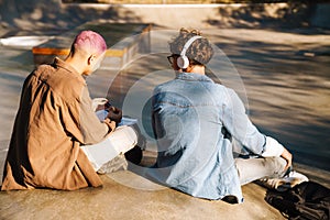 Two young stylish students boys sitting with backs to camera