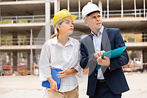 Two young successful architects on the construction site, discuss the construction plan