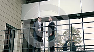 Two young successful businessmen walk through the porch to shake hands and greet each other