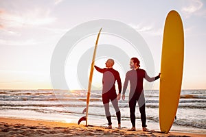 Two young surfers in black wetsuit with yellow surfing longboards on a ocean coast at sunset ocean. Water sport