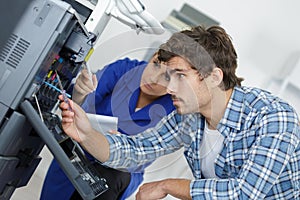Two young technicians repairing printer
