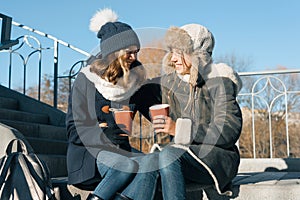 Two young teenage girls having fun outdoors, girlfriends in winter clothes, positive people and friendship concept. Girls drinking