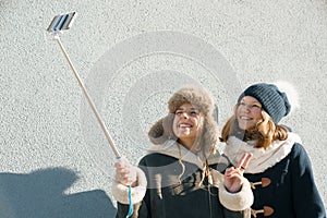 Two young teenage girls having fun outdoors, happy smiling girlfriends in winter clothes taking selfie, positive people and