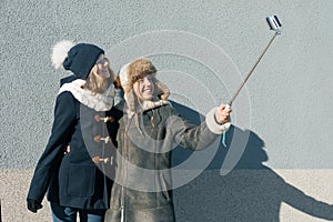 Two young teenage girls having fun outdoors, happy smiling girlfriends in winter clothes taking selfie, positive people and