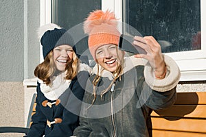 Two young teenage girls having fun outdoors, happy smiling girlfriends in winter clothes taking selfie, positive people and