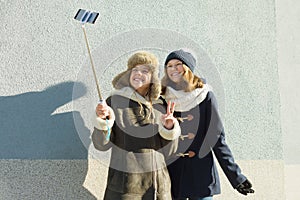 Two young teenage girls having fun outdoors, happy smiling girlfriends in winter clothes taking selfie, positive people and friend