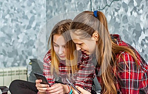 Two young teenage girls using mobile phones while sitting on a couch at home