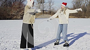 Two young woman in christmas hats rides ice skating and fells on ice