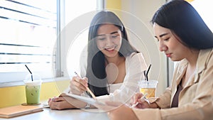 Two young woman working together on a digital tablet at modern cafe.