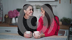 Two young woman friends drink tea in evening in kitchen, talk and have fun