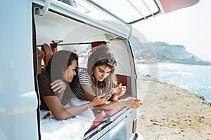 Two young woman lay down hold smartphone inside of retro van