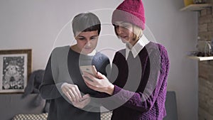 Two young woman looking mobile phone standing in room. Woman holding smartphone