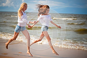 Two young woman running and having fun on the beach