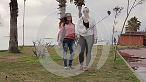 Two Young woman taking self portrait on the seafront using smartphone mobile cell phone camera.