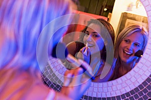 Two young women applying makeup in a nightclub