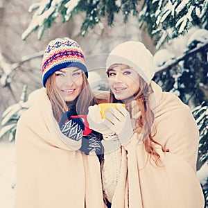 Two young women with colorful cups drinking tea outdoor and smiling