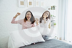 Two young women dance laughing together happy friendship smile with happiness in bedroom wear casual dress on bed. Happy girl