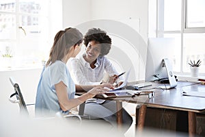 Two young women discussing documents at a desk in an office