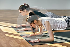 Two young women doing yoga asana Low Plank Pose
