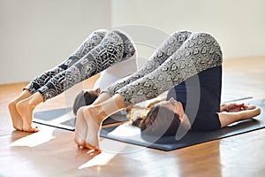 Two young women doing yoga asana plow pose