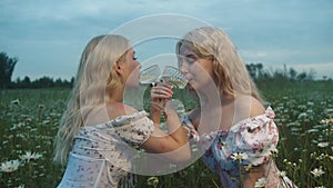 Two young women drink white wine in the field at the bruderschaft