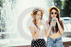 Two young women drinking colorful cocktails from bottles in the street. Outdoors lifestyle portrait