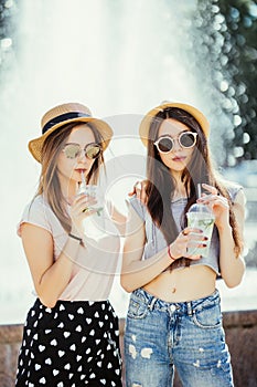 Two young women drinking colorful cocktails from bottles in the street. Outdoors lifestyle portrait
