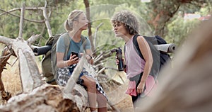 Two young women are engaged in conversation during a hike in a wooded area