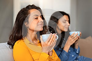 Two young women enjoying aroma of coffee holding cups indoors
