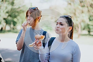 Two young women enjoying snacks in a sunny park setting, a moment of friendship and leisure