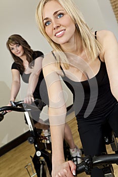 Two Young Women On Exercise Bikes At The Gym