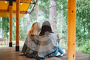 Two young women friends drinking tea and relaxing in glamping in the woods